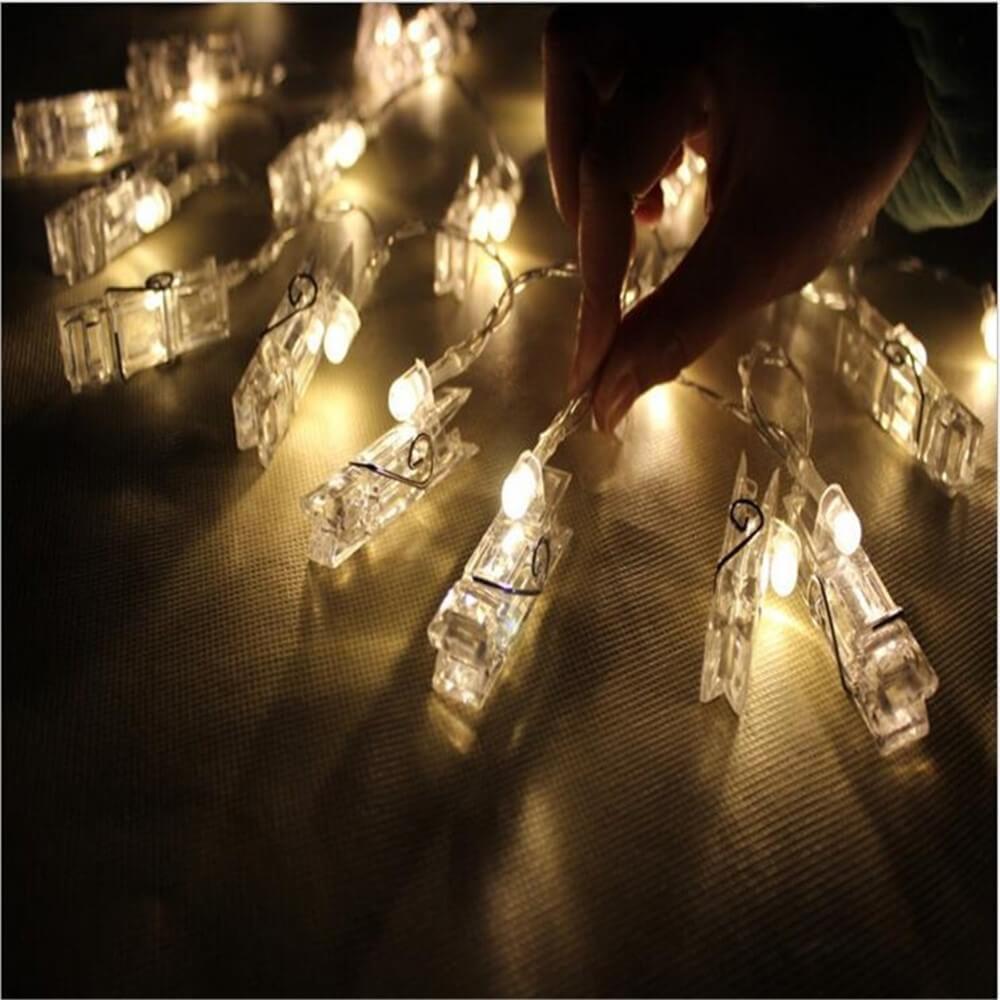 Eine Hand berührt die leuchtende Cover-Discount Lichterkette LED Fotoklammer, batteriebetrieben - ideal für stimmungsvolle Dekoration auf dunkler Oberfläche.