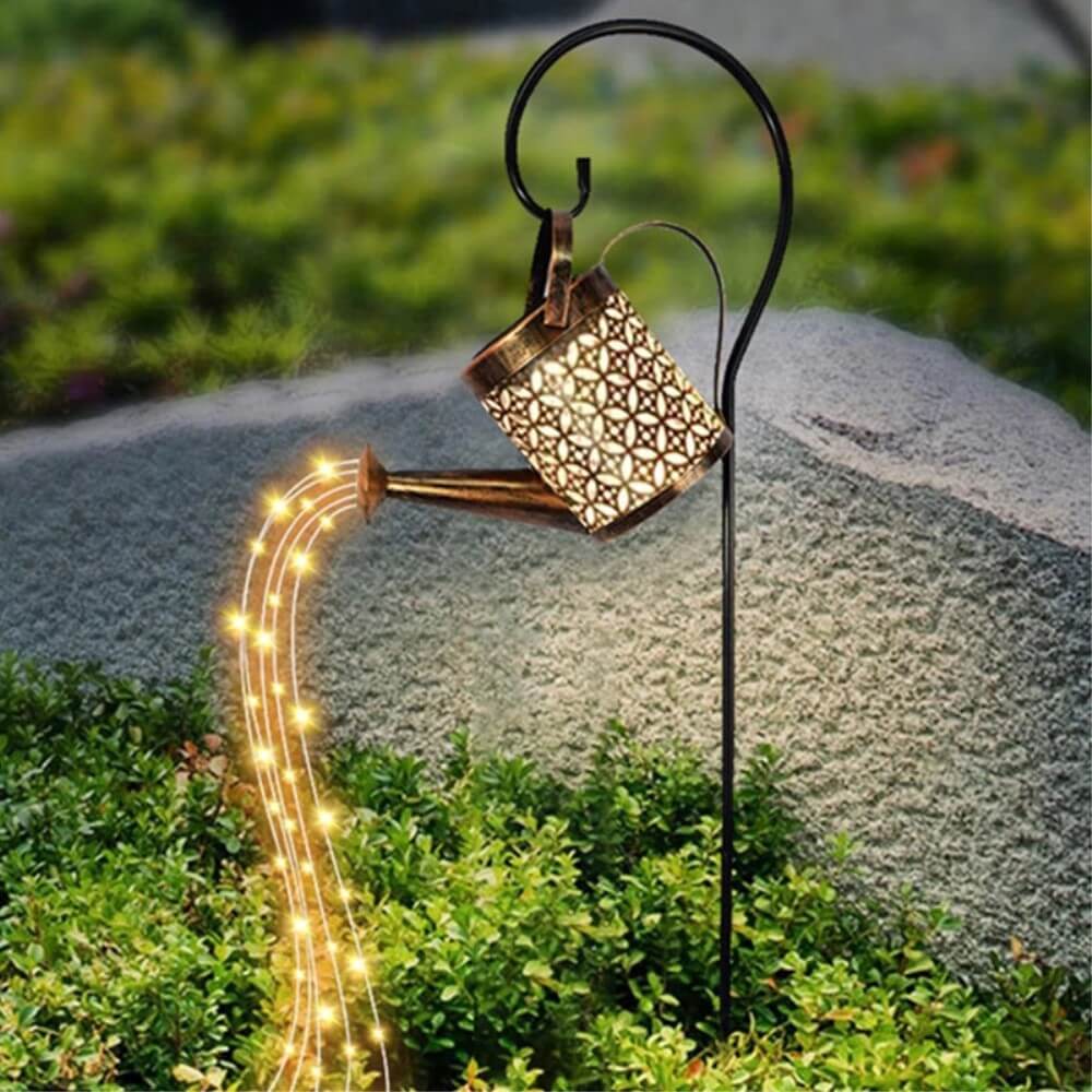 Der Cover-Discount Solar LED Gartenstecker Giesskanne ist eine Gartenleuchte in Form einer Metallgießkanne mit warmen LED-Lichterketten, die wie Wasser über Pflanzen und Steine fließen und mit Solartechnik betrieben werden, um ein bezauberndes, energieeffizientes Leuchten zu erzeugen.