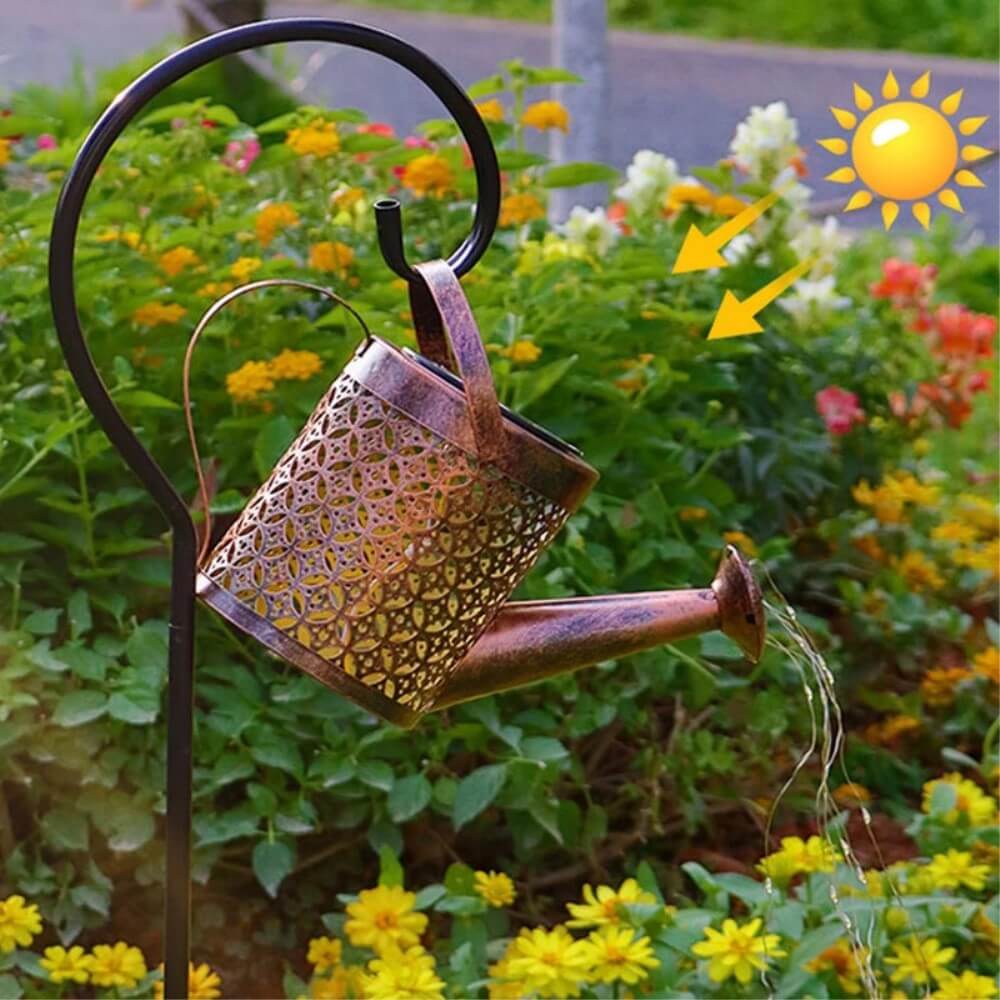 Der Cover-Discount Solar LED Gartenstecker Giesskanne hängt an einem Gartenhaken und wirft warmweißes Licht auf gelbe Blumen im hellen Sonnenlicht und schafft so eine gemütliche Gartenatmosphäre.