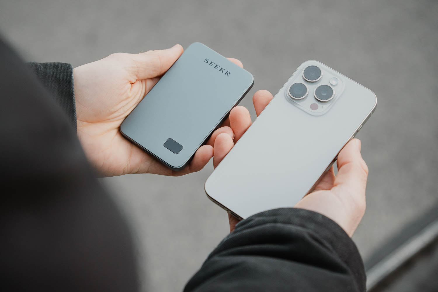 Eine Person hält ein SEEKR SWISS SEEKR Power Mag - Schwarz 5000 mAh mit ultradünnem Design in einer Hand und ein silbernes Smartphone in der anderen.