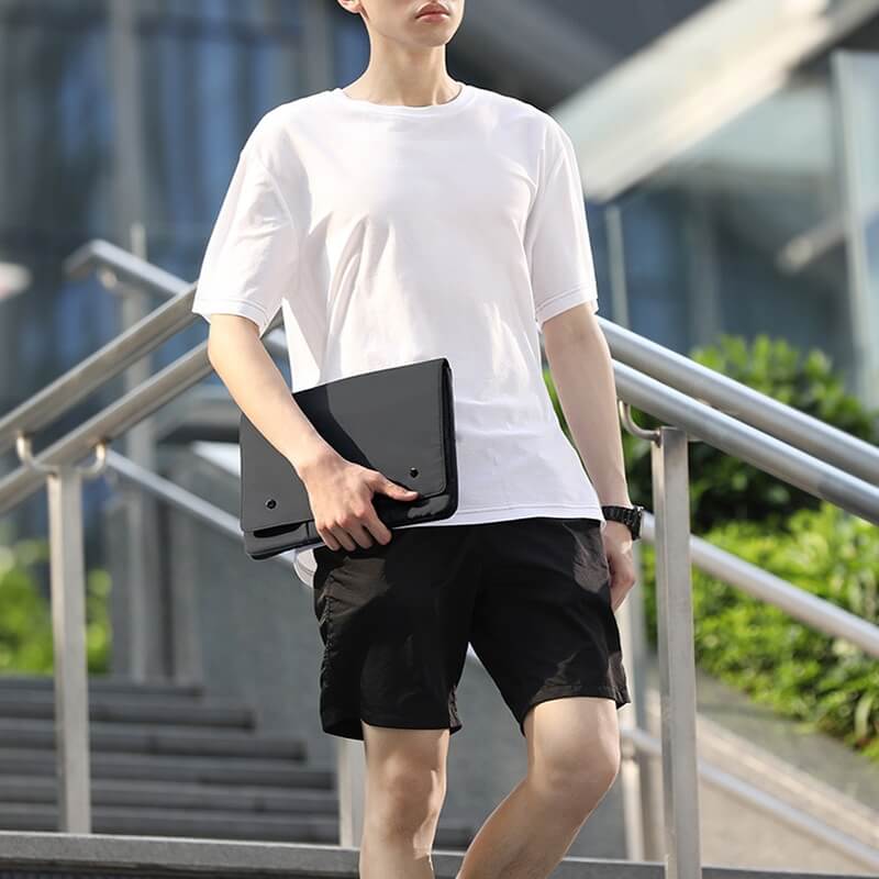 Person in weißem T-Shirt und schwarzen Shorts hält die Cover-Discount Laptop-Hülle Tasche für Notebook und geht eine Außentreppe hinunter.