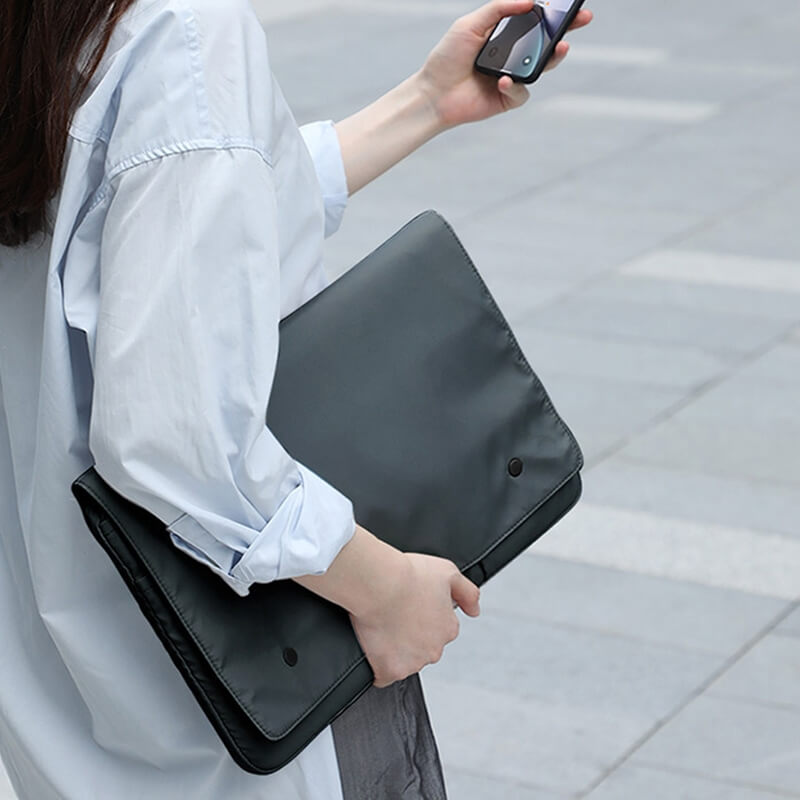Eine Person trägt eine Cover-Discount Laptop-Hülle Tasche für Notebook und ein Smartphone, während sie auf einem gepflasterten Bürgersteig geht.