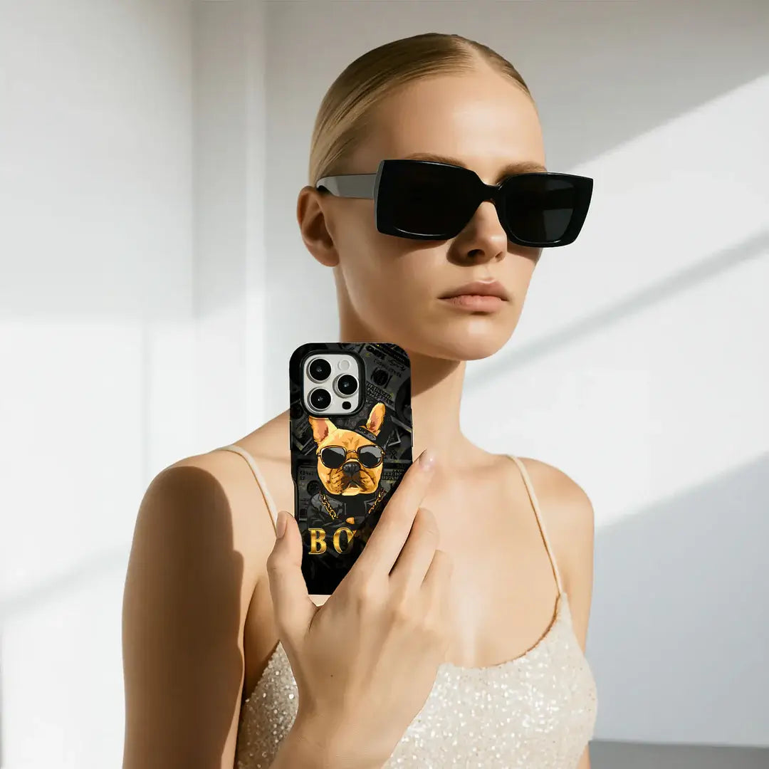 Eine Frau mit Sonnenbrille und Glitzerkleid zeigt ihr Galaxy S25 Ultra mit der Limited Edition Casarto Handyhülle Boss von Cover-Discount - einer MagSafe kompatiblen Hülle mit einem Hund mit Sonnenbrille.